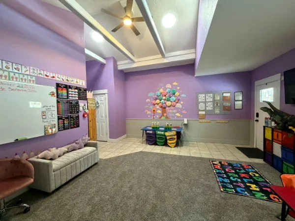 The whole classroom: whiteboard and calendar wall, reading couch, the You Belong Here tree, and the alphabet rug